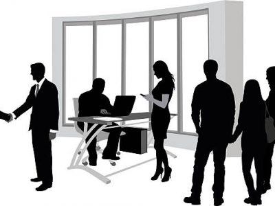 A vector silhouette illustration of a busy school office with several people going about their business including young men greeting shaking hands, a man working at a desk computer, a young woman using her cell phone, and a group of three male and female students standing and socializing.